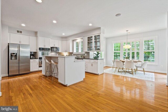kitchen featuring visible vents, appliances with stainless steel finishes, light wood-style floors, a breakfast bar, and white cabinetry