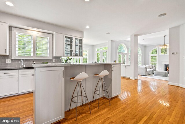 kitchen with white cabinets, light wood finished floors, a breakfast bar area, recessed lighting, and glass insert cabinets