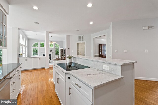 kitchen with visible vents, light wood-style floors, black electric stovetop, a center island, and white cabinetry