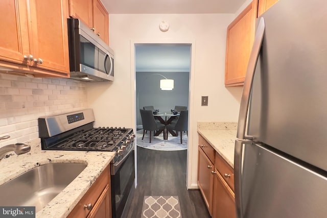 kitchen featuring light stone counters, a sink, stainless steel appliances, backsplash, and dark wood-style floors