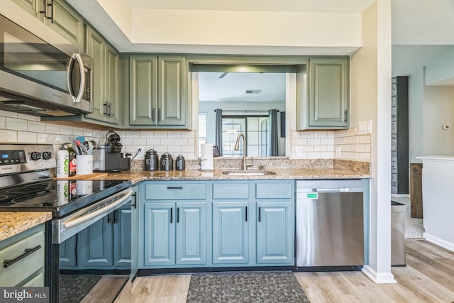 kitchen featuring a sink, green cabinetry, stainless steel appliances, and light wood-type flooring