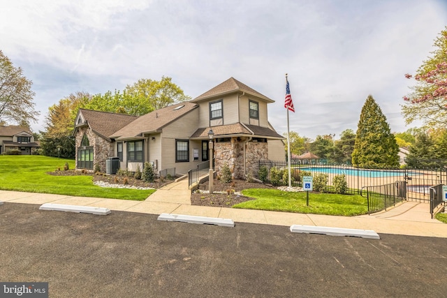 view of front of home with a community pool, fence, uncovered parking, a front lawn, and stone siding
