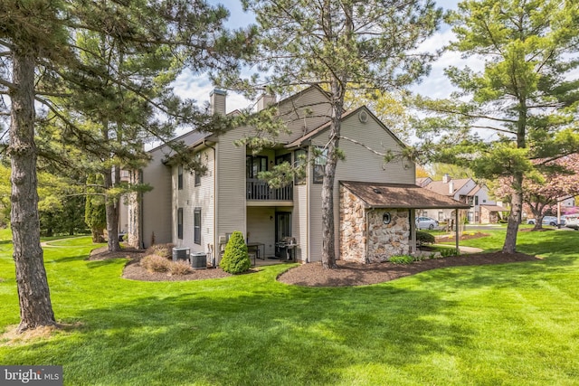 rear view of property with a yard, a chimney, a balcony, and stone siding