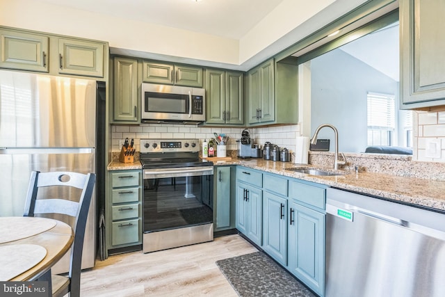 kitchen featuring light stone countertops, a sink, appliances with stainless steel finishes, backsplash, and green cabinets