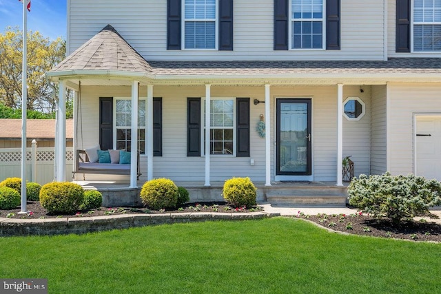 entrance to property with a porch, roof with shingles, fence, and a yard