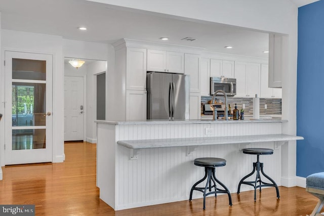 kitchen with white cabinetry, appliances with stainless steel finishes, a breakfast bar, and light wood-style floors