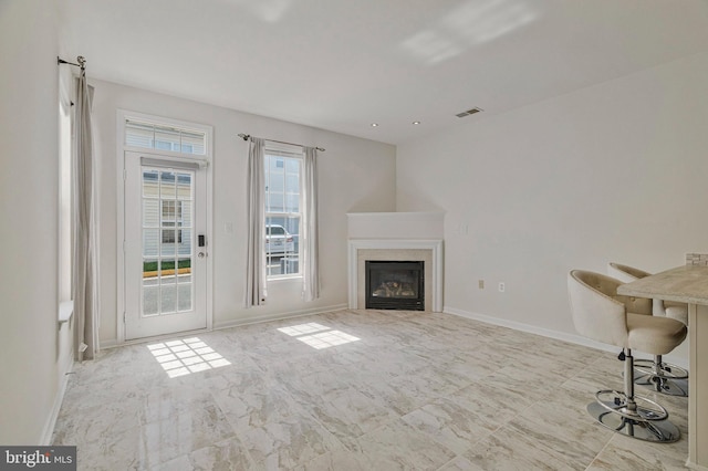 unfurnished living room with marble finish floor, baseboards, a glass covered fireplace, and visible vents