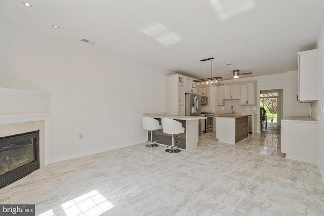 kitchen with a breakfast bar, a glass covered fireplace, stainless steel appliances, a kitchen island, and visible vents