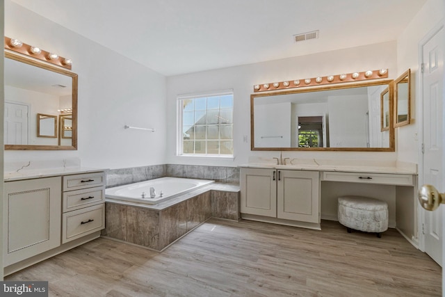 bathroom with a garden tub, visible vents, wood finished floors, two vanities, and a sink