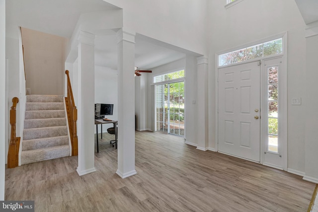 entryway with stairs, a towering ceiling, baseboards, ceiling fan, and light wood-type flooring