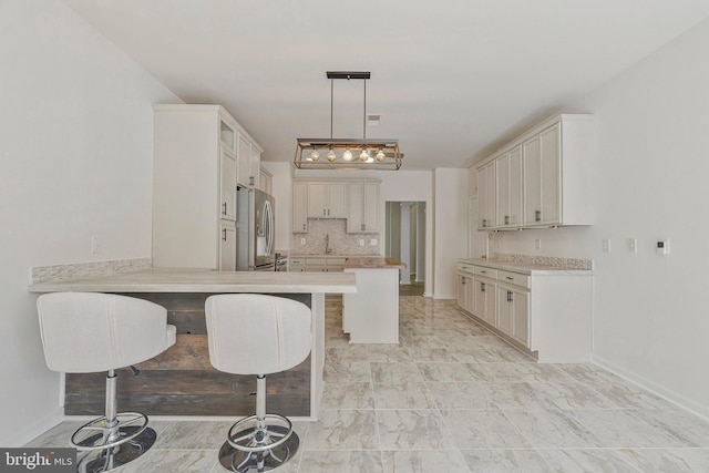 kitchen with a breakfast bar area, light countertops, a sink, a peninsula, and stainless steel fridge