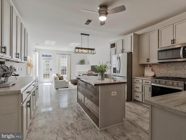 kitchen with a ceiling fan, backsplash, appliances with stainless steel finishes, marble finish floor, and open floor plan
