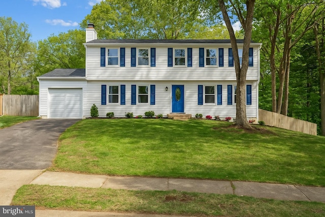 colonial home with a chimney, a front yard, a garage, fence, and aphalt driveway