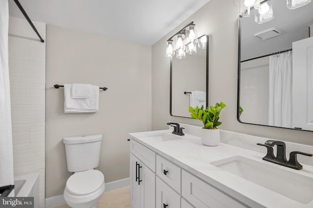 bathroom featuring double vanity, toilet, baseboards, and a sink