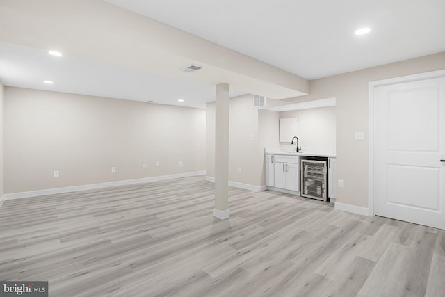finished below grade area featuring light wood-style flooring, indoor wet bar, baseboards, wine cooler, and visible vents