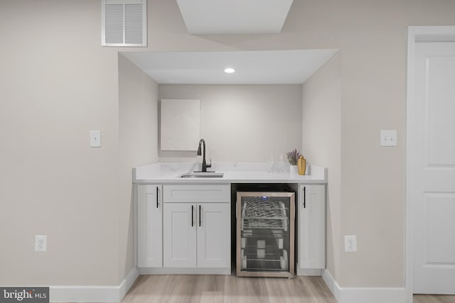 bar with visible vents, baseboards, light wood-style floors, beverage cooler, and a sink