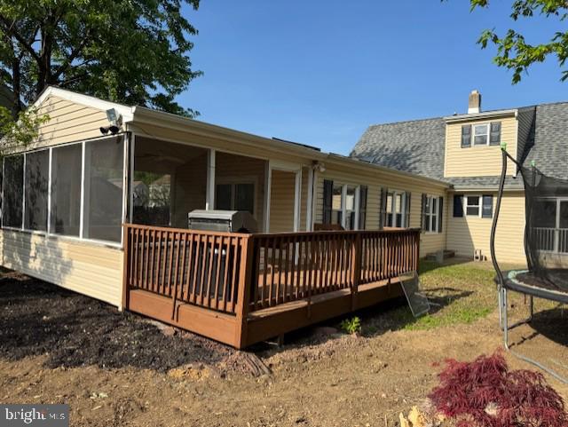 rear view of house featuring a trampoline, a chimney, a sunroom, and a deck