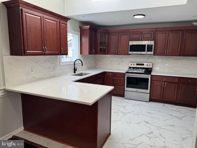 kitchen with appliances with stainless steel finishes, a sink, marble finish floor, a peninsula, and reddish brown cabinets