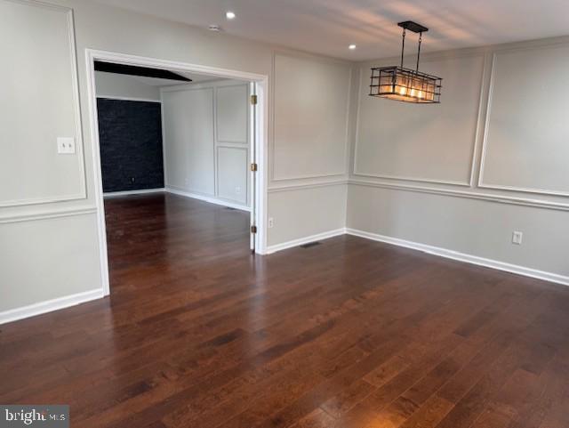 empty room featuring baseboards, recessed lighting, a decorative wall, and wood finished floors