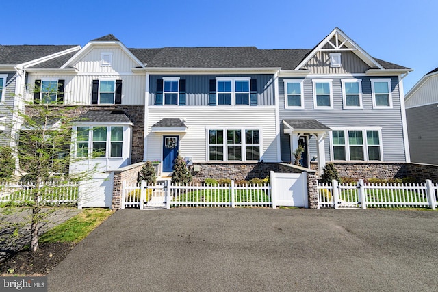 townhome / multi-family property with stone siding, a shingled roof, a gate, board and batten siding, and a fenced front yard