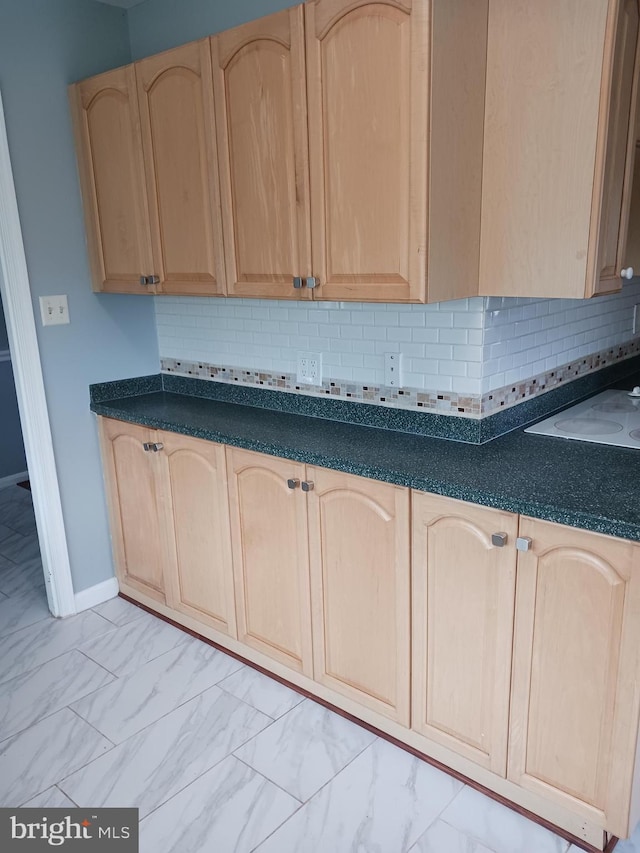 kitchen with marble finish floor, light brown cabinetry, dark countertops, and tasteful backsplash