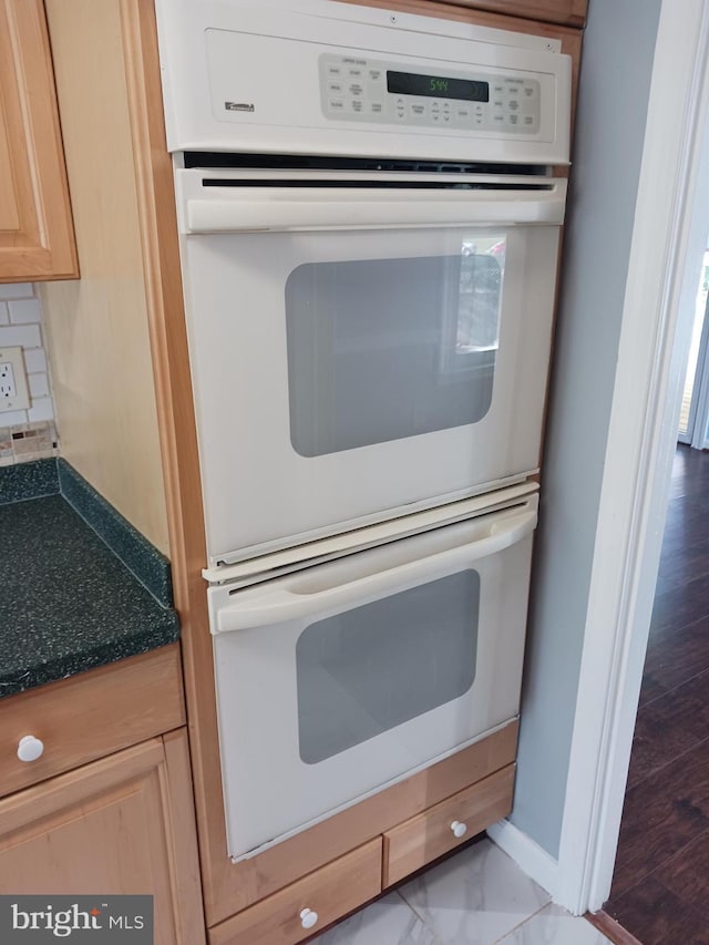 details with light brown cabinetry, dark countertops, white double oven, baseboards, and backsplash