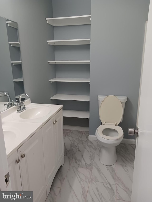 bathroom with double vanity, a sink, baseboards, toilet, and marble finish floor