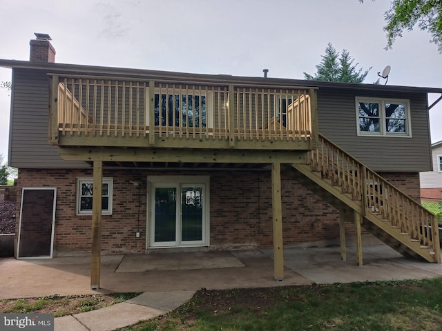 rear view of house featuring brick siding, a chimney, a patio, and stairs