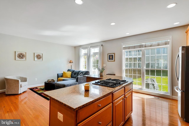 kitchen with freestanding refrigerator, a kitchen island, open floor plan, light wood-type flooring, and black gas stovetop