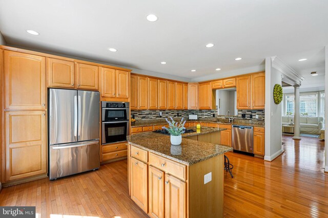 kitchen with stainless steel appliances, dark stone countertops, light wood finished floors, and a center island