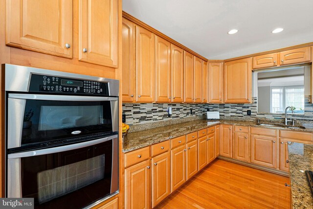 kitchen featuring backsplash, stainless steel double oven, a sink, stone counters, and light wood-style flooring