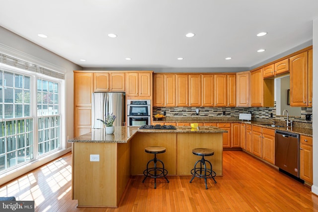 kitchen featuring appliances with stainless steel finishes, a sink, light wood finished floors, tasteful backsplash, and a kitchen island