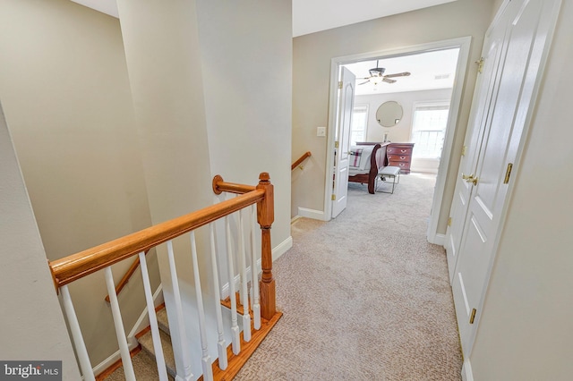 hall with light colored carpet, baseboards, visible vents, and an upstairs landing