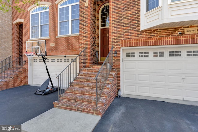 view of exterior entry featuring brick siding, aphalt driveway, and a garage