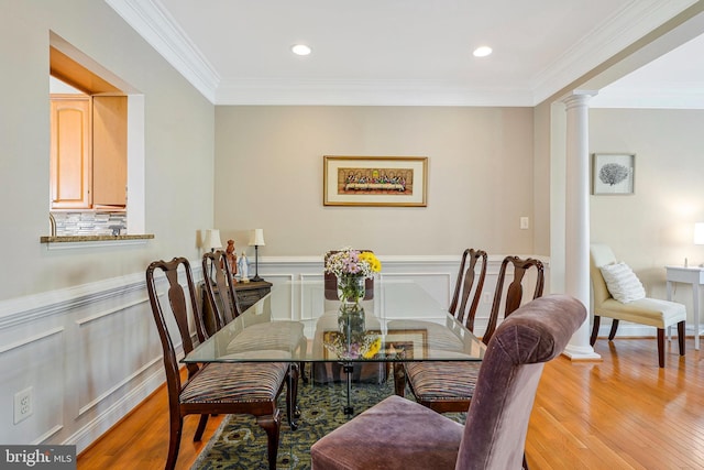 dining room featuring crown molding, decorative columns, light wood finished floors, and wainscoting