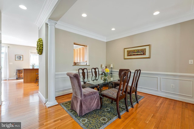dining room with crown molding, ornate columns, light wood-style flooring, and a wainscoted wall