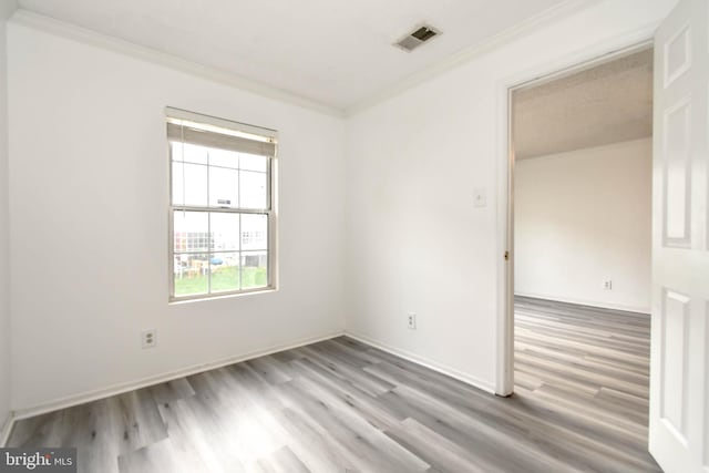 spare room featuring crown molding, baseboards, wood finished floors, and visible vents