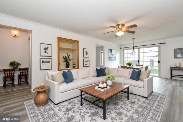 living room featuring light wood-type flooring, baseboards, crown molding, and ceiling fan with notable chandelier