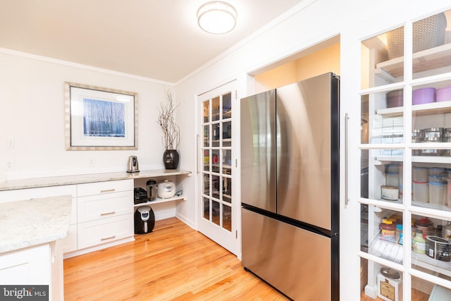 kitchen with white cabinets, light stone counters, light wood finished floors, freestanding refrigerator, and ornamental molding