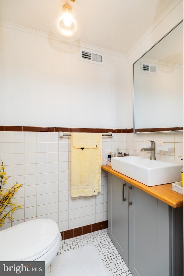 half bathroom featuring visible vents, vanity, toilet, and tile walls