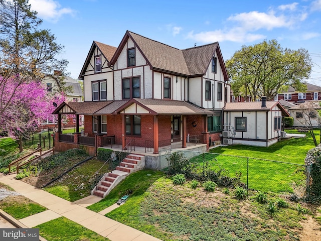tudor-style house with fence private yard, a front yard, stucco siding, brick siding, and a shingled roof