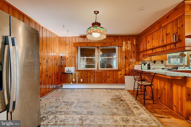 kitchen featuring a breakfast bar area, wood walls, wood finished floors, a baseboard heating unit, and stainless steel fridge
