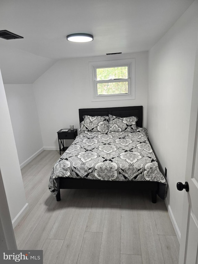 bedroom with baseboards, vaulted ceiling, wood finished floors, and visible vents