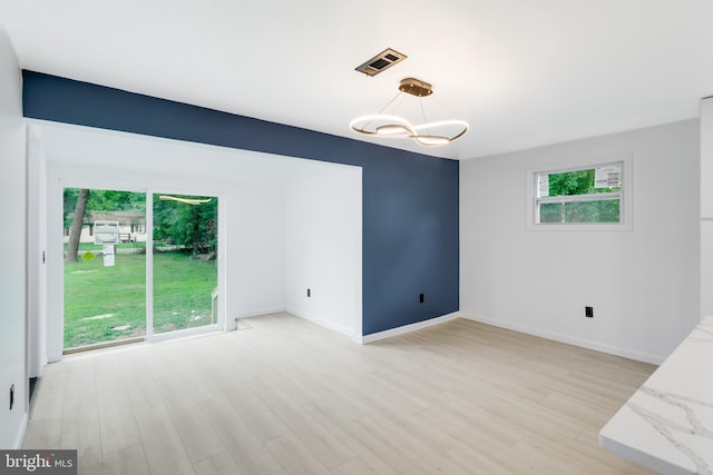 unfurnished room with an inviting chandelier, light wood finished floors, baseboards, and visible vents