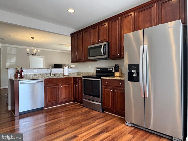 kitchen with a notable chandelier, stainless steel appliances, a peninsula, dark wood-type flooring, and ornamental molding