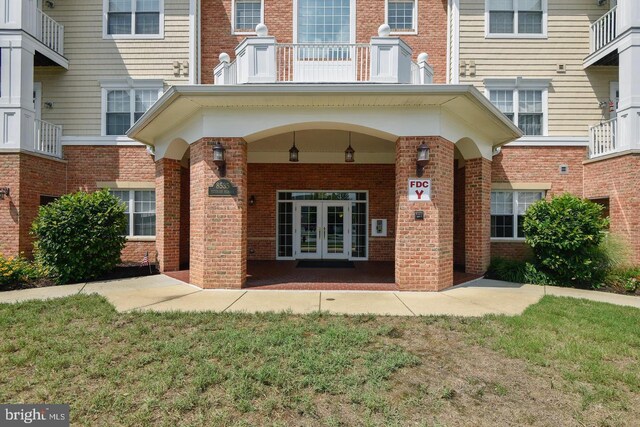 entrance to property with french doors, a balcony, and brick siding