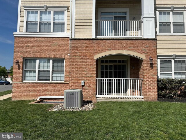 exterior space featuring a lawn, cooling unit, brick siding, and a balcony