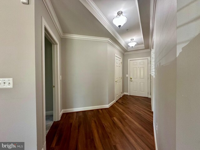 hallway with baseboards, ornamental molding, a tray ceiling, and dark wood-type flooring