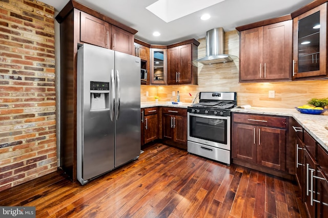 kitchen featuring appliances with stainless steel finishes, light stone counters, wall chimney exhaust hood, dark wood-type flooring, and a skylight