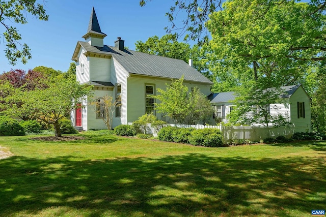 view of side of home with a lawn, fence, a chimney, and metal roof